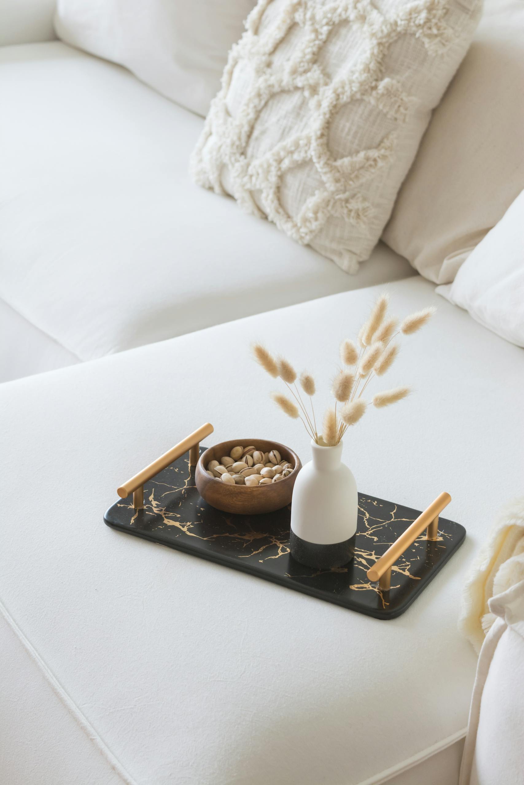 A cozy white sofa with a black marble tray featuring a vase and nuts, perfect for modern home decor.