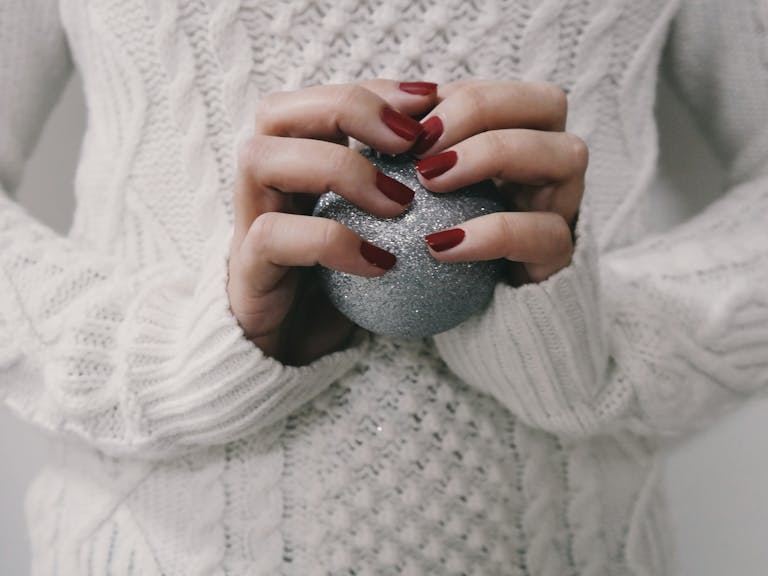 Classy winter nail colors demonstrated on hands with a dark red manicure holding a silver glitter ball.