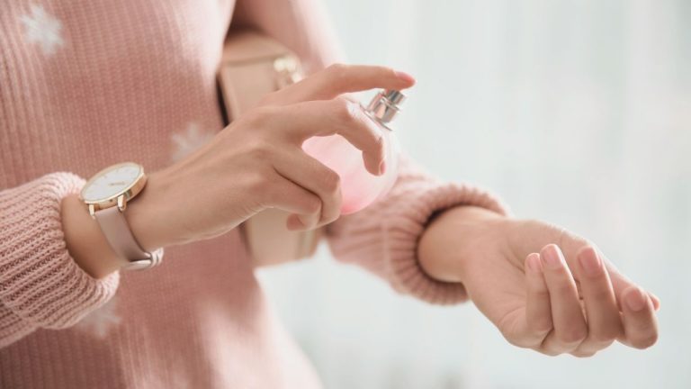 cozy winter perfume being sprayed onto a woman's wrist in a soft luxe sweater.