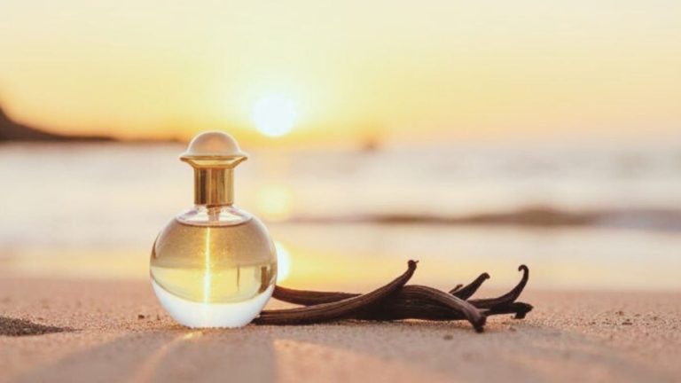A luxe glass bottle of soft summer vanilla perfume on a beach at golden hour adorned by vanilla beans.