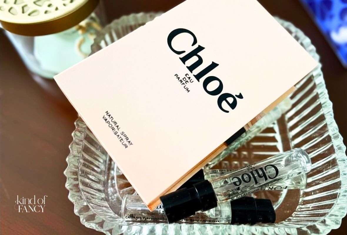 Closeup of a sample size of soft rose perfume, Chloe EDP, in a delicate glass tray on a wooden dresser.