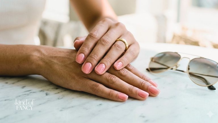 warm pink jelly nails summer manicure on woman's hands next to aviator sunglasses on a marble table
